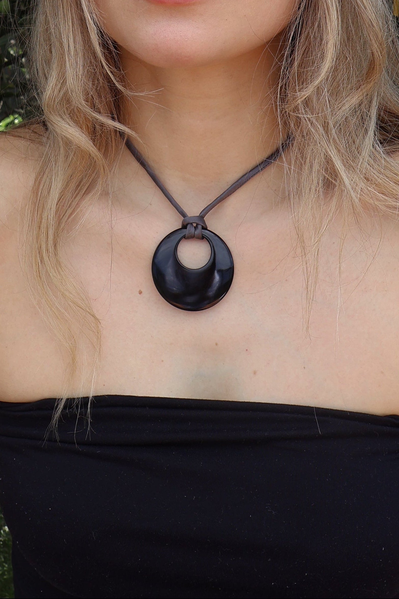 Woman wearing a black top and necklace with greenery in the background